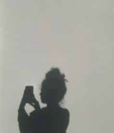 the shadow of a woman taking a photo with her cell phone in front of a white wall