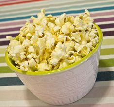 a bowl filled with popcorn sitting on top of a striped table cloth next to a cup