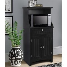 a black cabinet with a microwave on top and a potted plant next to it