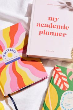 three books sitting on top of a bed next to an orange and pink book bag