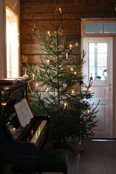 a small christmas tree with lights is next to a piano in a room that has wood paneling