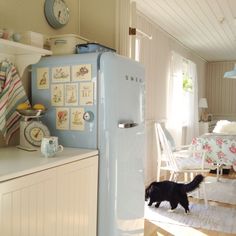 a black cat walking across a kitchen floor next to a blue refrigerator freezer oven