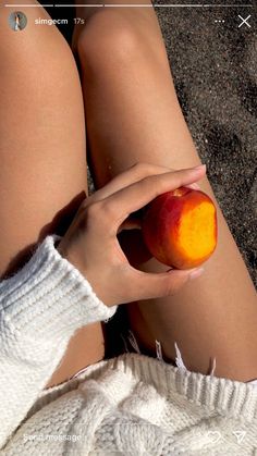 a woman is holding an apple in her hand while sitting on the ground with her legs crossed