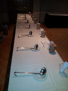 a long table with spoons, cups and napkins laid out on top of it