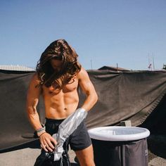 a man with no shirt standing next to a trash can and looking down at his pants