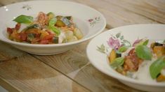 two white bowls filled with food sitting on top of a wooden table next to each other