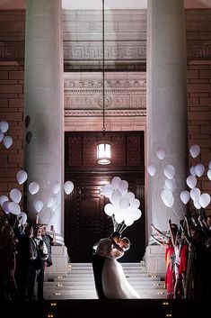 a bride and groom standing in front of a building with balloons floating from the ceiling