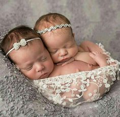 two newborn babies are cuddling together in a basket on a bed with white lace