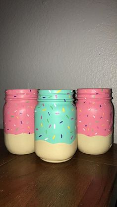 three jars with sprinkles painted on them are sitting on a wooden table