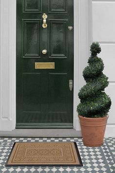 a green door with two potted plants next to it and a welcome mat on the ground