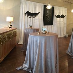 a table with silver cloth on it in front of two white drapes and a black moustache