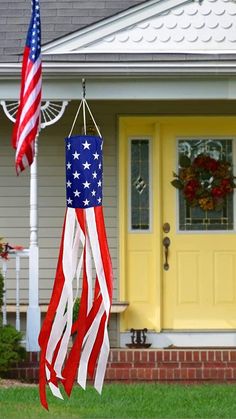 two american flags are hanging from a pole in front of a house with yellow doors