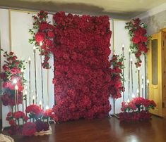 a room with red flowers and candles on the wall next to it is a large piece of art made out of wood