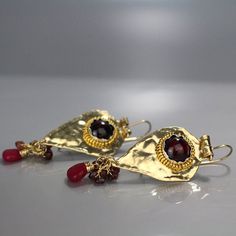 Garnet Bohemian Earrings, Gold Garnet Earrings, Protection Earrings, Deep Red Earrings, Gift for Mom, Spiritual Jewelry, Meaningful Gifts These protection earrings are made in an organic gold filled shaped, similar to a knight's shield and have natural garnets set within. These earrings have a strong spiritual meaning and are meant to protect its wearer. An old technique was used for this piece: foil inlay and hand-hinge integration. A unique style of silver bezel setting showcases the garnet ge Artisan Red Teardrop Earrings, Red Garnet Teardrop Earrings, Red Teardrop Garnet Earrings, Gold Garnet Teardrop Earrings, Gold Teardrop Garnet Earrings, Artisan Red Drop Earrings, Handmade Ruby Dangle Earrings, Unique Red Brass Earrings, Handmade Ruby Teardrop Earrings