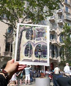 a person holding up a piece of art in front of a building with many windows