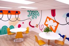 an office decorated with colorful wallpaper and art work on the walls, including round tables and chairs