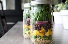 two mason jars filled with salads sitting on top of a wooden table