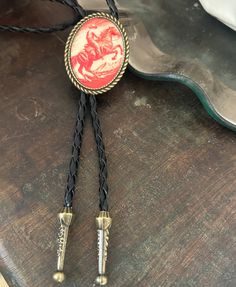 This awesome bolo tie has a vintage cowboy print with a clear resin coating and metal backing. Handmade in our shop! The cord is black and genuine leather. Our bolos pair nicely with many of our belt buckles! They make wonderful gifts. The western bolo tie rope length is 39' ; pendant size is 1 1/2'' x 1 1/4'' Vintage Adjustable Bolo Ties, Vintage Black Bolo Ties For Gift, Vintage Black Bolo Ties As Gift, Vintage Black Jewelry For Western-themed Events, Adjustable Black Bolo Tie For Rodeo, Black Adjustable Bolo Ties For Rodeo, Adjustable Black Bolo Ties For Rodeo, Vintage Bolo Tie With Adjustable Length For Western Events, Vintage Bolo Ties With Adjustable Length For Western-themed Events