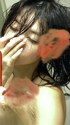 a woman holding her face to her nose while looking into a mirror with red paint on it