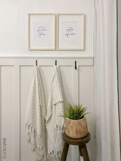 two framed pictures hang on the wall next to a wooden stool with a plant in it