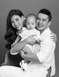 a man holding a baby while sitting on top of a chair next to a woman