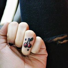 a woman's hand with a cherry and star tattoo on her thumb, holding onto the finger of another person