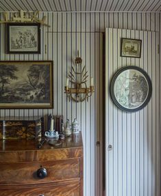 a room with striped walls and pictures on the wall, along with a wooden dresser