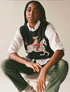 a woman sitting on top of a white toilet wearing green pants and a sweater vest