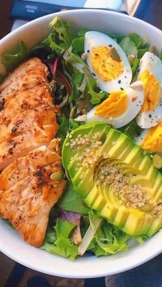 a salad with salmon, avocado and hard boiled eggs in it on a table