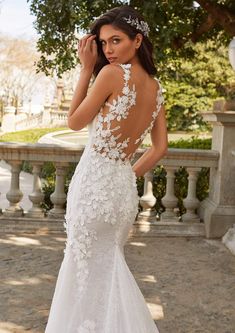 a woman in a white wedding dress with flowers on it's back, posing for the camera