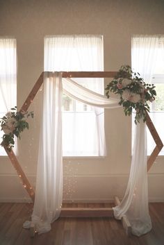 an arch decorated with flowers and lights in front of a window on a wooden floor