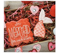 an open box filled with cookies and other items on top of a wooden table next to a sign that says we mermaid for each other