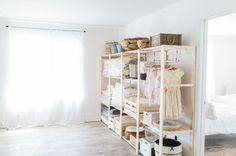 a bedroom with white walls and wooden shelves filled with clothes, bags and other items