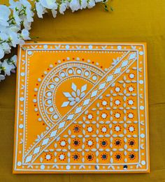 an orange and white decorative plate with flowers on the table next to it, in front of a yellow background