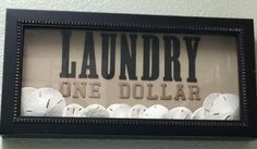 a sign that reads laundry one dollar hanging on the wall above toilet paper rolls in a black frame