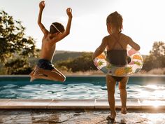 two children jumping in the air near a swimming pool