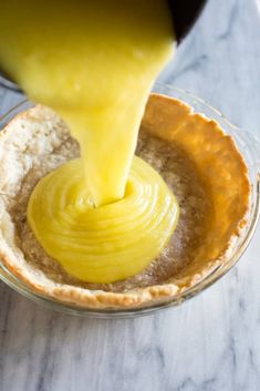 someone pouring sauce into a pie crust in a glass bowl