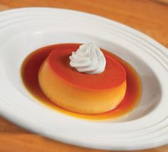 a small dessert on a white plate with whipped cream and orange sauce in the center