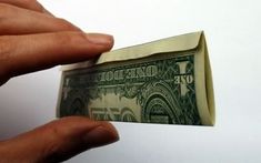 a hand holding a folded dollar bill in front of a white background with the word $ 10 printed on it