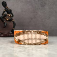 an orange and white beaded bracelet sitting on top of a table next to a statue