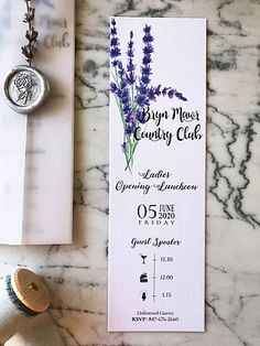 a bottle of wine next to a purple flower on a white marble counter top with a wax stamp