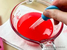 a person is mixing red liquid in a glass bowl with a blue plastic spoon and measuring tape