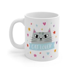 a white coffee mug with a cat face and stars around it that says cat lover