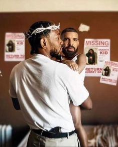 a man holding a child in his arms with posters on the wall behind him