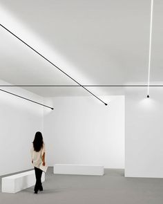 a woman is standing in an empty room with white walls and black wires hanging from the ceiling