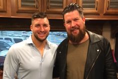 two men standing next to each other in front of a kitchen counter with wooden cabinets