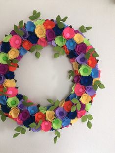 a colorful wreath made out of felt flowers on a white wall next to a clock