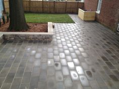 a brick patio in the middle of a yard with trees and grass behind it, next to a fence