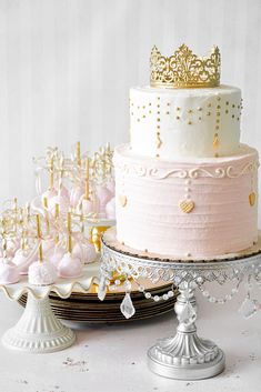 three tiered cake with pink frosting and gold crown on top, surrounded by other desserts