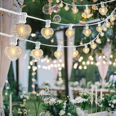 an outdoor wedding with lights strung from the ceiling and flowers in vases on the table